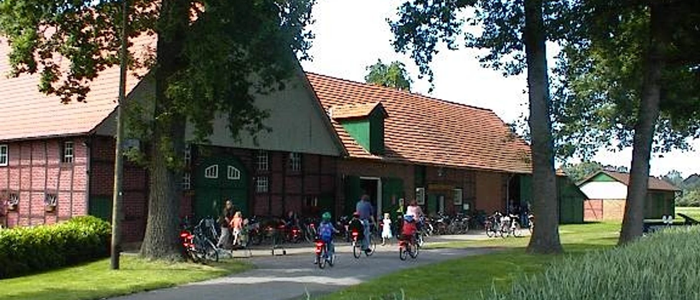 Das Heimatmueseum am Hühnermoor in Marienfeld Eine Gruppe von Radfahrern vor einem großen roten Backsteingebäude in einer grünen Landschaft.