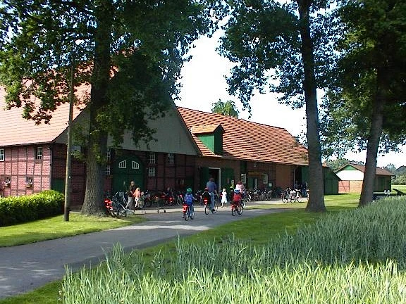 Das Heimatmueseum am Hühnermoor in Marienfeld Eine Gruppe von Radfahrern vor einem großen roten Backsteingebäude in einer grünen Landschaft.