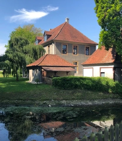 Bürgerbegegnungsstätte Haus Werther Historisches Gebäude mit roten Ziegeldächern am Ufer eines Wassergrabens, umgeben von Bäumen.
