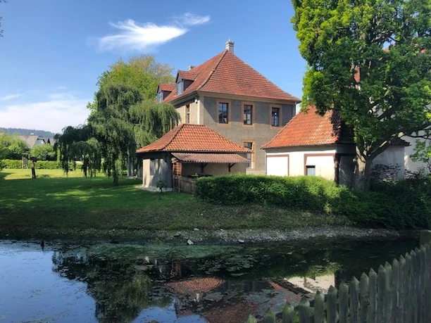 Bürgerbegegnungsstätte Haus Werther Historisches Gebäude mit roten Ziegeldächern am Ufer eines Wassergrabens, umgeben von Bäumen.