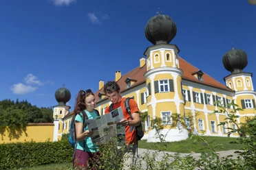Schloss Ramspau Zwei Personen mit Karte vor dem gelben Schloss Ramspau, blauer Himmel.