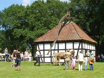 Menschen genießen das LandArt Festival beim Fachwerkhaus auf dem Museumshof Rahden, umgeben von Bäumen.