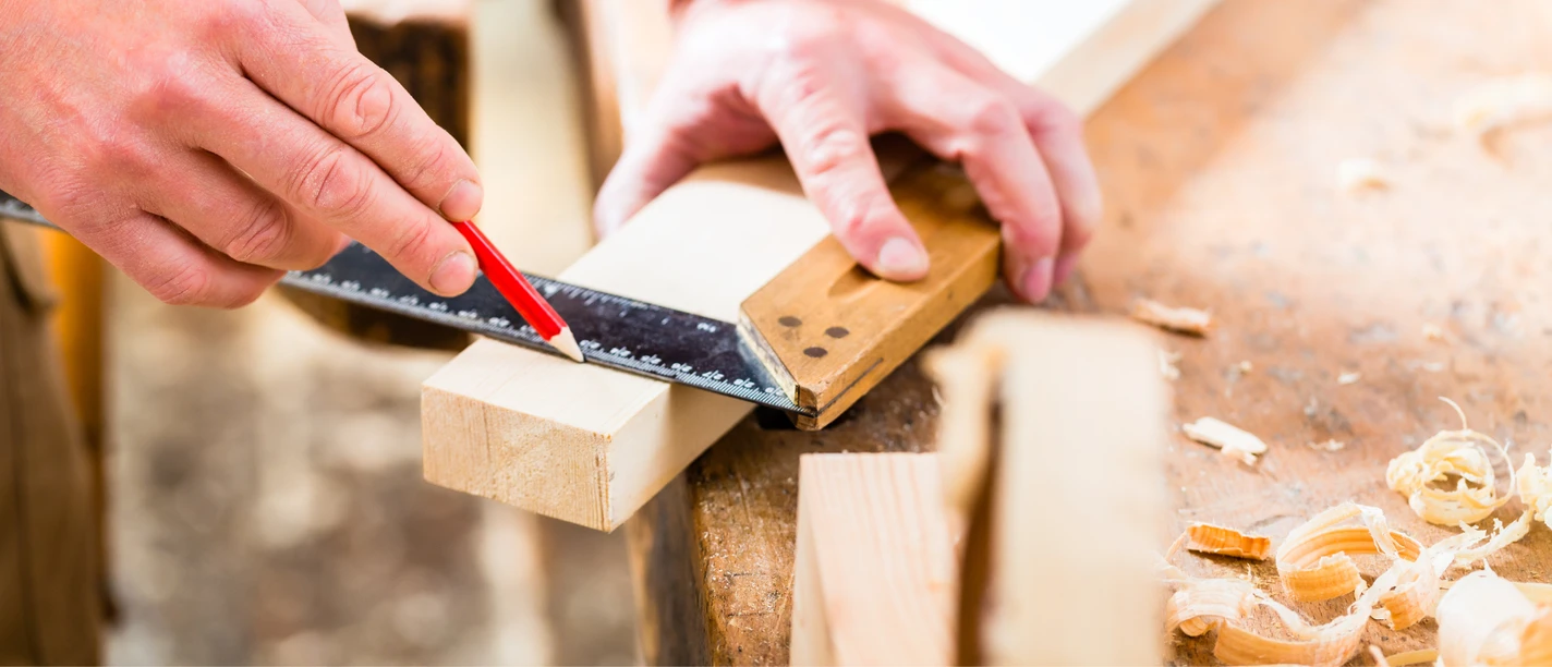 Wahrzeichen aus Holz(resten) Hände markieren mit Bleistift und Winkelmaß ein Holzstück auf der Werkbank.