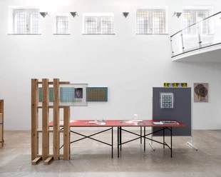 Coloan-Oskar-Lee-Edit Heller Ausstellungsraum mit Installationen, roten Tischen und hohen Fenstern