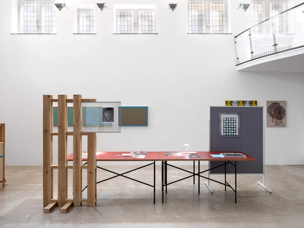 Coloan-Oskar-Lee-Edit Heller Ausstellungsraum mit Installationen, roten Tischen und hohen Fenstern