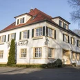 Außenaufnahme Landgasthof Potthoff, Borgholzhausen-Barnhausen Zweistöckiges weißes Gebäude mit roten Ziegeldach und grünen Fensterläden an einem sonnigen Tag.