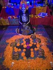 dia de Muertos Geschminkte Catrina vor farbenreichem Tag-der-Toten-Altar mit Blumen und Totenköpfen