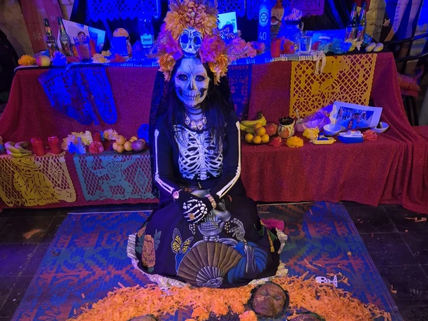 dia de Muertos Geschminkte Catrina vor farbenreichem Tag-der-Toten-Altar mit Blumen und Totenköpfen