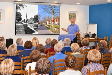 Pressefoto.jpg Vortrag zur Ortsgeschichte mit Publikum und historischem Bildvergleich auf Leinwand.