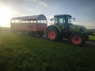 Wolle's Eventfahrten Grüner Traktor mit rotem Planwagen auf Feldweg bei tief stehender Sonne