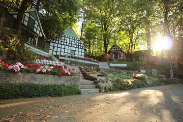 Freilichtbühne Kahle Wart Fachwerkhäuser umgeben von blühenden Blumen und Bäumen auf einer Freilichtbühne bei Sonnenuntergang.
