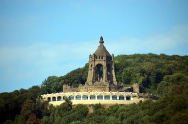 Kaiser-Wilhelm-Denkmal mit Ringterrasse Das Kaiser-Wilhelm-Denkmal ragt imposant über eine bewaldete Landschaft mit blauer Himmelskulisse.