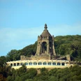 Kaiser-Wilhelm-Denkmal mit Ringterrasse Das Kaiser-Wilhelm-Denkmal ragt imposant über eine bewaldete Landschaft mit blauer Himmelskulisse.
