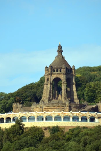Kaiser-Wilhelm-Denkmal mit Ringterrasse Das Kaiser-Wilhelm-Denkmal ragt imposant über eine bewaldete Landschaft mit blauer Himmelskulisse.