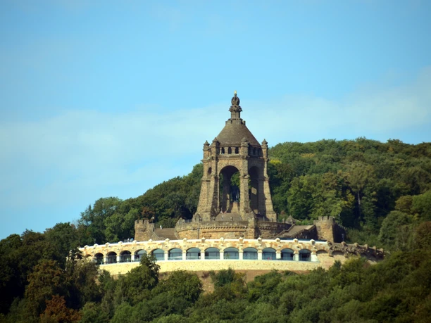 Kaiser-Wilhelm-Denkmal mit Ringterrasse Das Kaiser-Wilhelm-Denkmal ragt imposant über eine bewaldete Landschaft mit blauer Himmelskulisse.