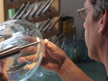 Glashütte Gernheim: Glasbe- und Verarbeitung Glasbläser bearbeitet mit Präzision ein heißes Glasobjekt, umgeben von Werkzeugen in der Werkstatt.