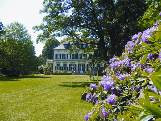Historisches Rittergut mit großem Garten, umgeben von blühenden Rhododendren und alten Bäumen.