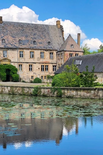 Wasserschloss Tatenhausen Historische Wasserschlossanlage mit malerischem Teich, umgeben von Bäumen und blühenden Seerosen.