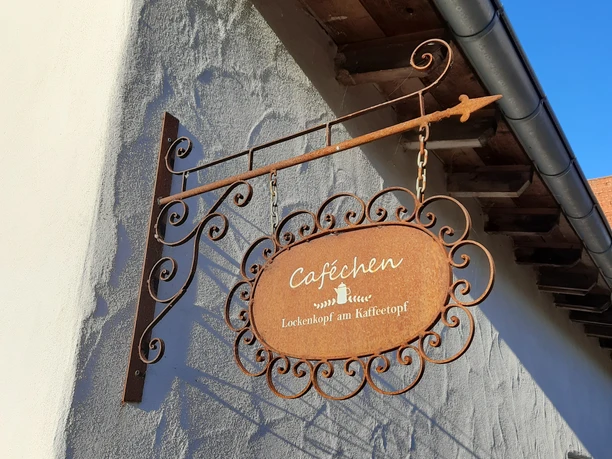 Lockenkopf am Kaffeepott Zu sehen ist das Ladenschild, mit den Schriftzug "Caféchen - Lockenkopf am Kaffeepott". Schild ist rustikal gestaltet und im Edelrostdesign.