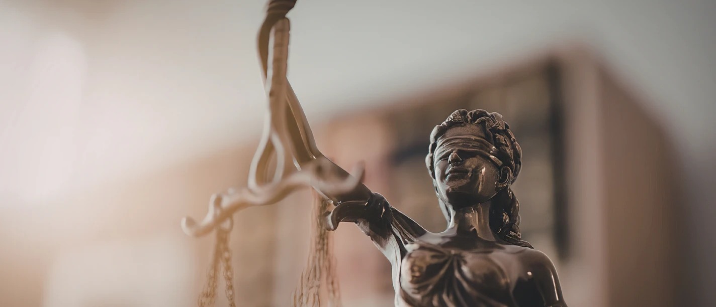 Justitia-Figur Justitia-Figur mit Augenbinde und Waage vor unscharfem Hintergrund.