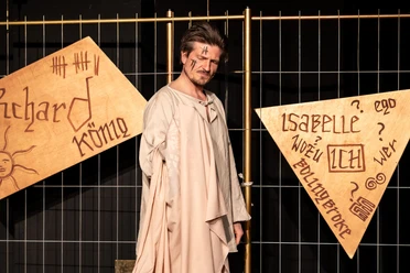 Richard II. - Solo eines Königs Schauspieler als Richard II. vor Bühnenzaun und beschrifteten Holztafeln