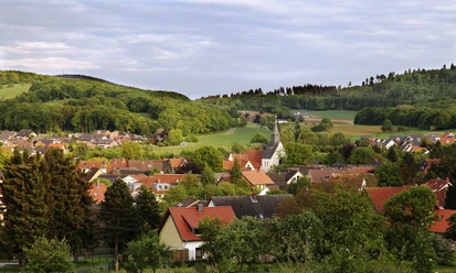 Borgholzhausen Ein idyllisches Dorf mit Kirchturm, umgeben von grünen Feldern und bewaldeten Hügeln im Hintergrund.
