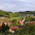 Borgholzhausen Ein idyllisches Dorf mit Kirchturm, umgeben von grünen Feldern und bewaldeten Hügeln im Hintergrund.