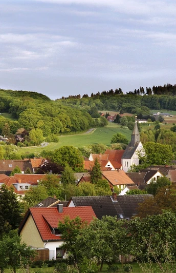 Borgholzhausen Ein idyllisches Dorf mit Kirchturm, umgeben von grünen Feldern und bewaldeten Hügeln im Hintergrund.