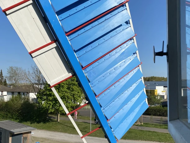 Blau-weißer Flügel der Windmühle Paula, fotografiert aus einem geöffneten Fenster.