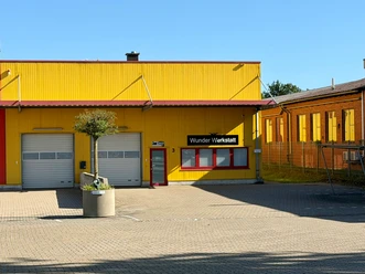 Wonder Workshop 1.jpg The yellow facade of the Wunder Werkstatt, with garage doors and a paved forecourt.