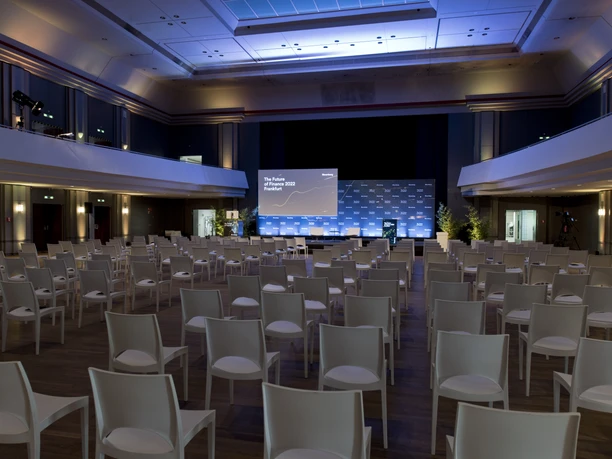 Zoo Gesellschaftshaus Frankfurt_Large Event Hall at the Zoo Gesellschaftshaus A large event hall at the Zoo Gesellschaftshaus in Frankfurt, featuring a stage, row seating, and blue event lighting. On the stage is a conference backdrop bearing the inscription “The Future of Finance 2022 Frankfurt.”