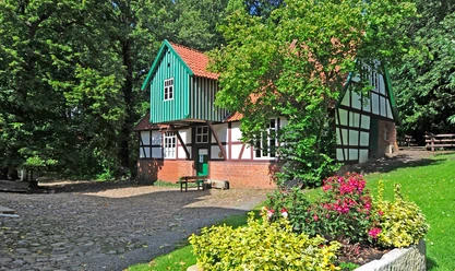 Wassermühle Döhren Historische Wassermühle mit roten Ziegelsteinmauern, Fachwerk und grünem Schindeldach im Grünen.