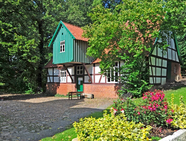 Wassermühle Döhren Historische Wassermühle mit roten Ziegelsteinmauern, Fachwerk und grünem Schindeldach im Grünen.