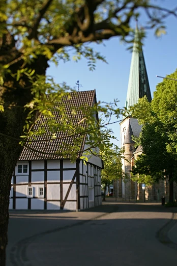 Café zur Linde und die Kirche St. Lambertus Langenberg Fachwerkhaus „Café zur Linde“ neben der steilen Kirchturmspitze der St. Lambertus-Kirche, umrahmt von Bäumen.