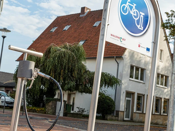 Luftpumpe Radroute Rund um Wallenhorst Fahrrad-Reparaturstation mit Pumpe vor einem roten Ziegeldach-Haus.
