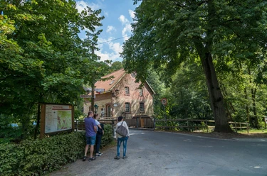 Knollmeyers Mühle Alte Backsteinmühle umgeben von Bäumen mit drei Spaziergängern auf der Landstraße.