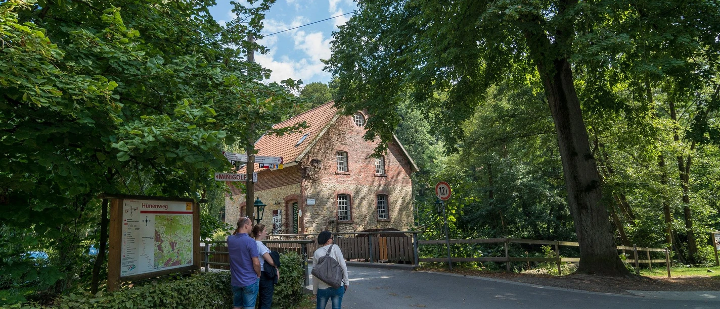 Knollmeyers Mühle Old brick mill surrounded by trees with three walkers on the country road.