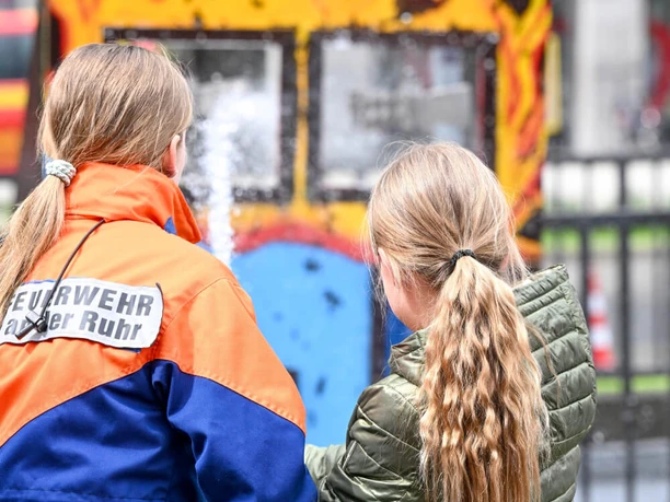 Blaulichttag – Mülheim mittendrin, Mülheim an der Ruhr Feuerwehrkraft und Kind üben am Löschschlauch vor einer Flammenkulisse