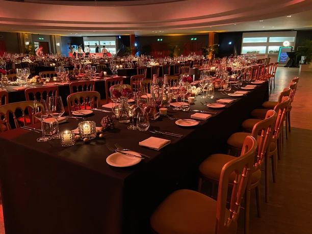 BALZER & Co. GmbH_Event Catering_Veranstaltungssaal Veranstaltungssaal mit langen gedeckten Banketttischen, Kerzen, Gläsern, Tellern und dekorativen Elementen. Der Raum ist stimmungsvoll beleuchtet und für ein Abendessen oder Event-Catering vorbereitet.