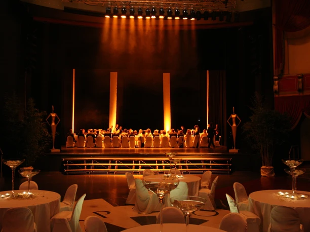 BALZER & Co. GmbH_MICE Agentur_Industrielle Eventlocation Industrielle Eventlocation mit Buffetstationen, Barbereichen, Stehtischen und farbiger Veranstaltungsbeleuchtung. Mehrere Personen bereiten oder betreuen das Catering im Raum.