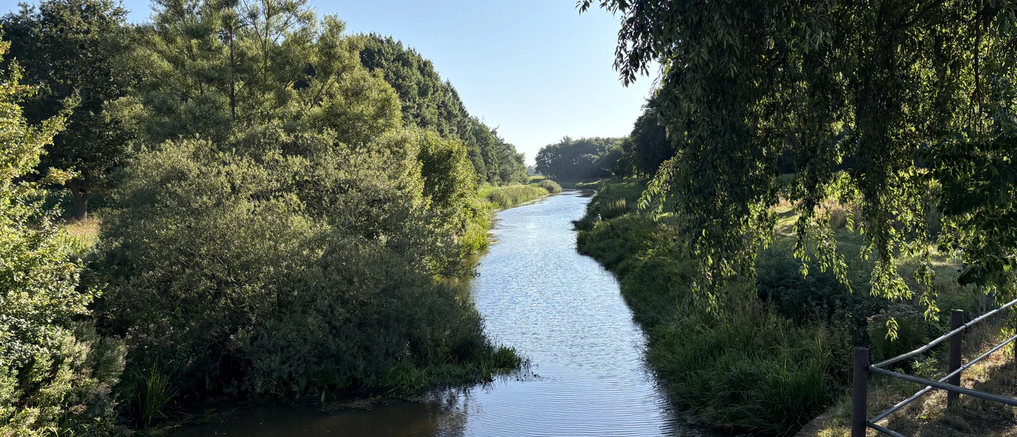 Wehr Varrel (4).jpeg Große Aue am Wehr Varrel, von Bäumen gesäumt, unter blauem Himmel.