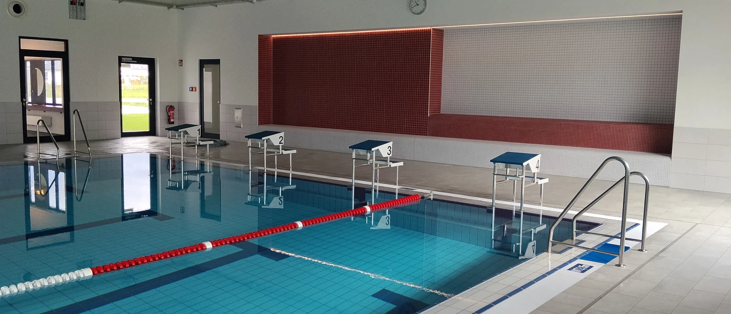 Hallenbad in Beverungen Innenansicht des Hallenbades mit einem Schwimmbecken, vier Startblöcken und einer Sitzbank.