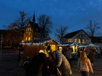 Weihnachtsmarkt in Apen.jpeg Weihnachtsmarkt in Apen mit beleuchteten Holzhütten vor Kirche bei Dämmerung.