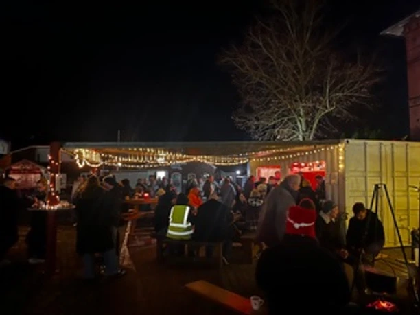 Abendstimmung auf dem Weihnachtsmarkt.jpeg Abendlicher Weihnachtsmarkt in Apen mit Lichterketten, Buden und Besuchergruppen.