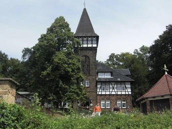 Sigwardsweg Historischer Fachwerkbau mit markantem Turm, umgeben von Bäumen, vor sonnigem Himmel.