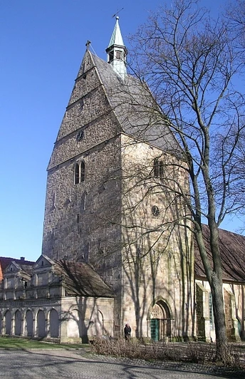 Archidiakonatskirche Apelern Mittelalterliche Kirche mit massivem Turm und spitzem Dach, umgeben von Bäumen, bei klarem Himmel.
