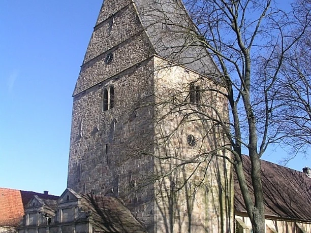 Archidiakonatskirche Apelern Mittelalterliche Kirche mit massivem Turm und spitzem Dach, umgeben von Bäumen, bei klarem Himmel.