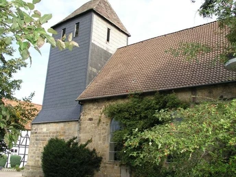 Rodenberg Kirche mit dunklem Schieferdach und historischem Bruchsteinturm umgeben von Bäumen und Sträuchern.