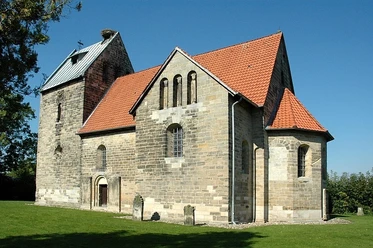 Sigwardskirche Romanische Kirche aus Naturstein mit rotem Ziegeldach, umgeben von Grünfläche und Bäumen.