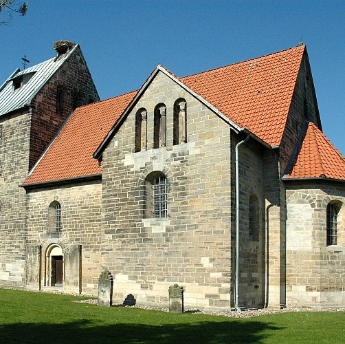 Sigwardskirche Romanische Kirche aus Naturstein mit rotem Ziegeldach, umgeben von Grünfläche und Bäumen.
